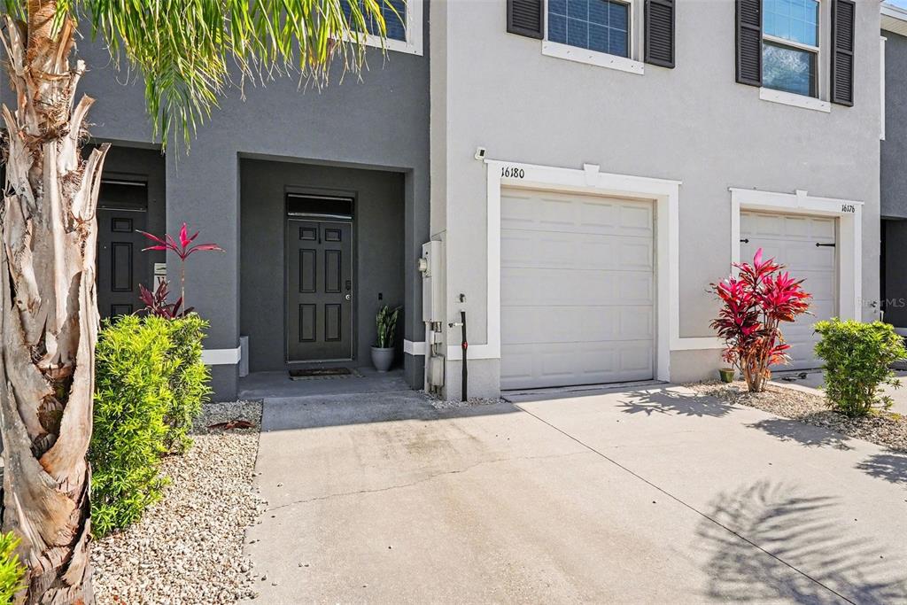 The exterior of a two-story townhouse features a gray garage, a dark front door, and landscaping — 16180 GLOWING GROVE AVENUE, ODESSA, FL