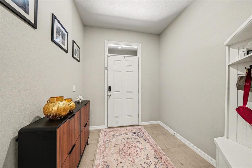 An entryway features a white door, a wooden console table, a patterned rug, and wall art — 16180 GLOWING GROVE AVENUE, ODESSA, FL