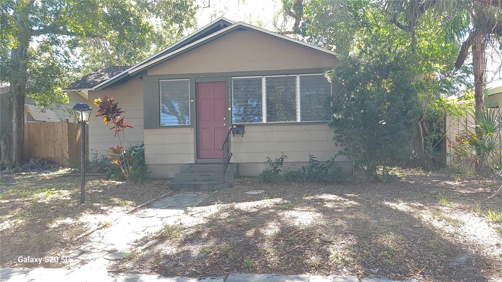 A single-story house with a red door, horizontal siding, and a front yard with trees — 3940 BURLINGTON AVENUE N, ST PETERSBURG, FL