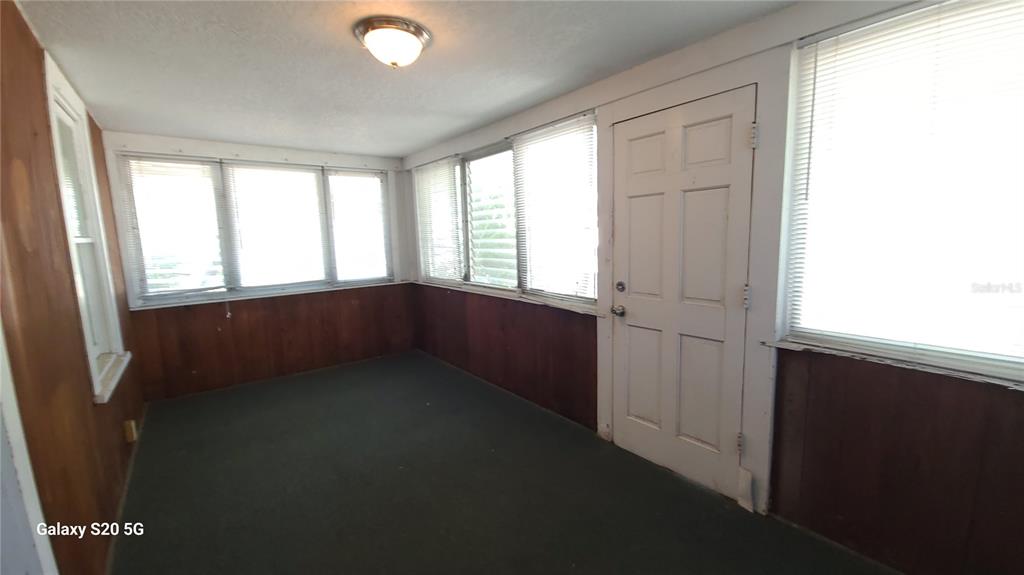A sunroom with wood paneling, green carpeting, multiple windows with blinds, and a white door — 3940 BURLINGTON AVENUE N, ST PETERSBURG, FL