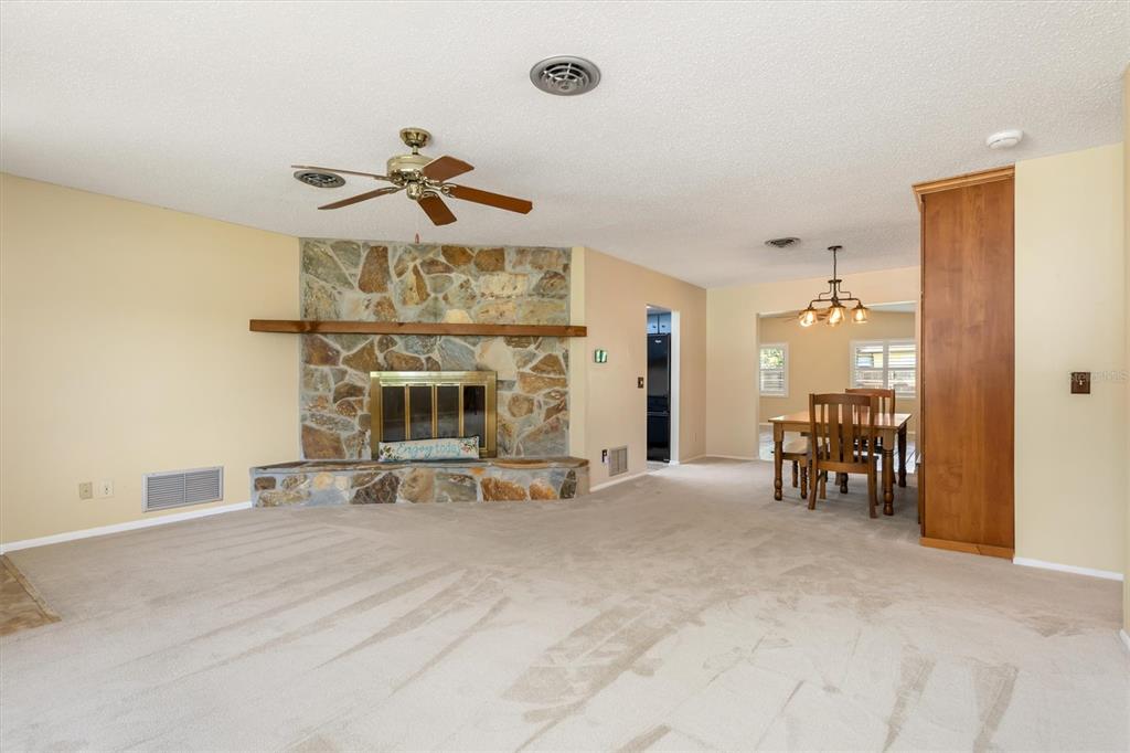 A living room with a stone fireplace, beige carpet, and an adjacent dining area — 1505 PINE STREET E, NOKOMIS, FL