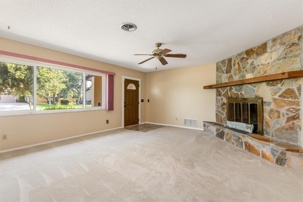 A living room features beige carpet, a stone fireplace, a ceiling fan, and a front door — 1505 PINE STREET E, NOKOMIS, FL