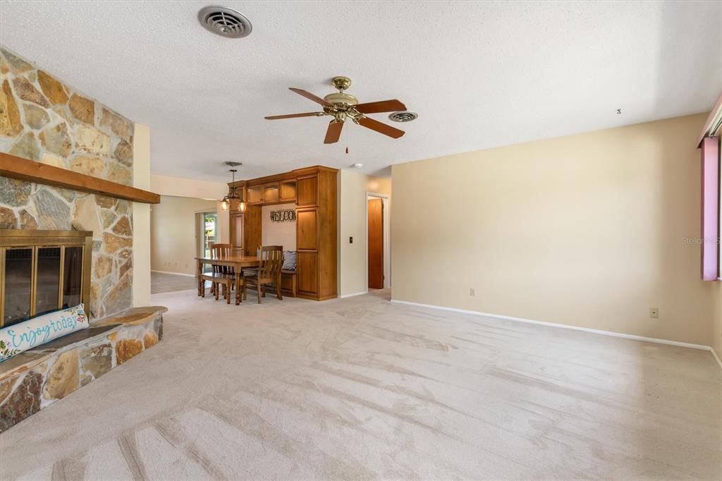 A living room with a stone fireplace, beige carpet, and a built-in dining area — 1505 PINE STREET E, NOKOMIS, FL