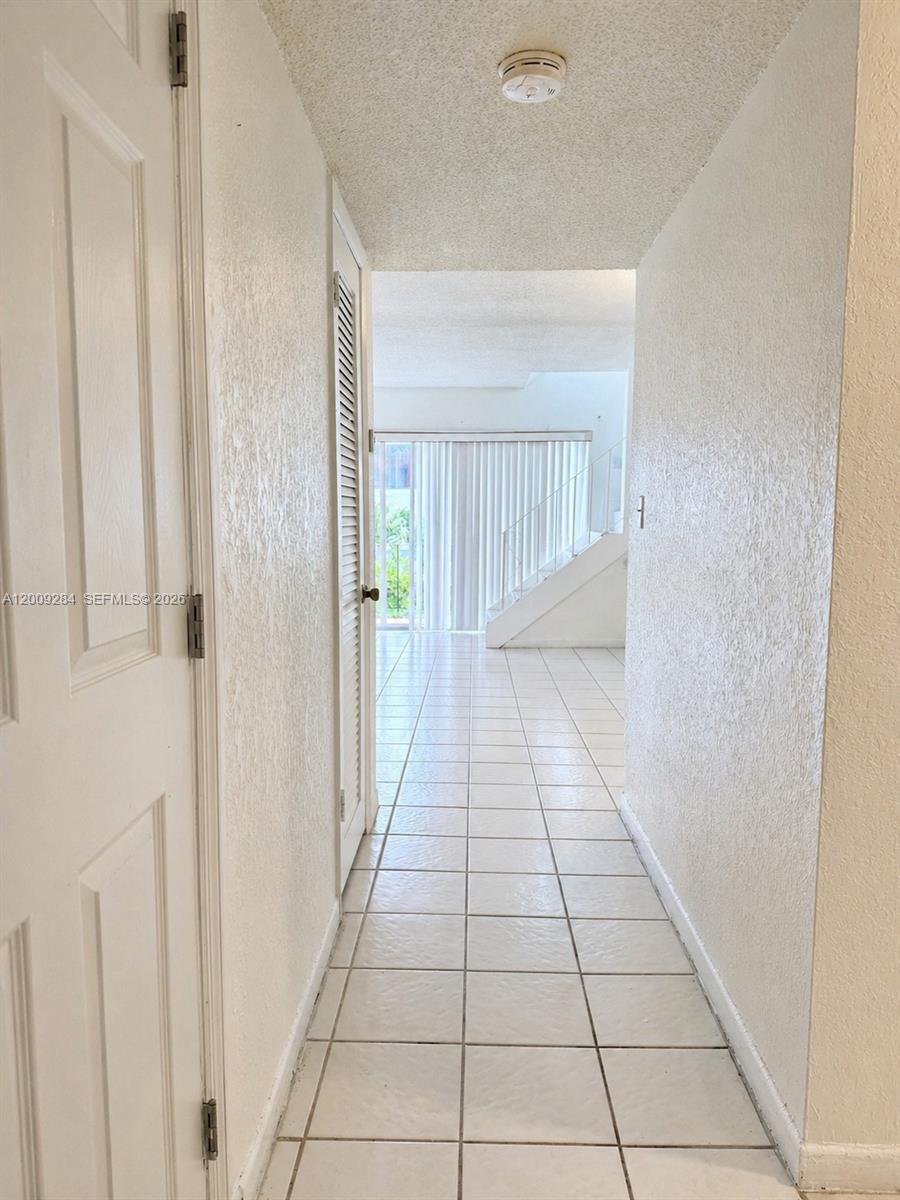 A tiled hallway leads toward a living area with a staircase and sliding glass doors — 1300 W 47th Pl # 218A, Hialeah FL 33012, HIALEAH, FL