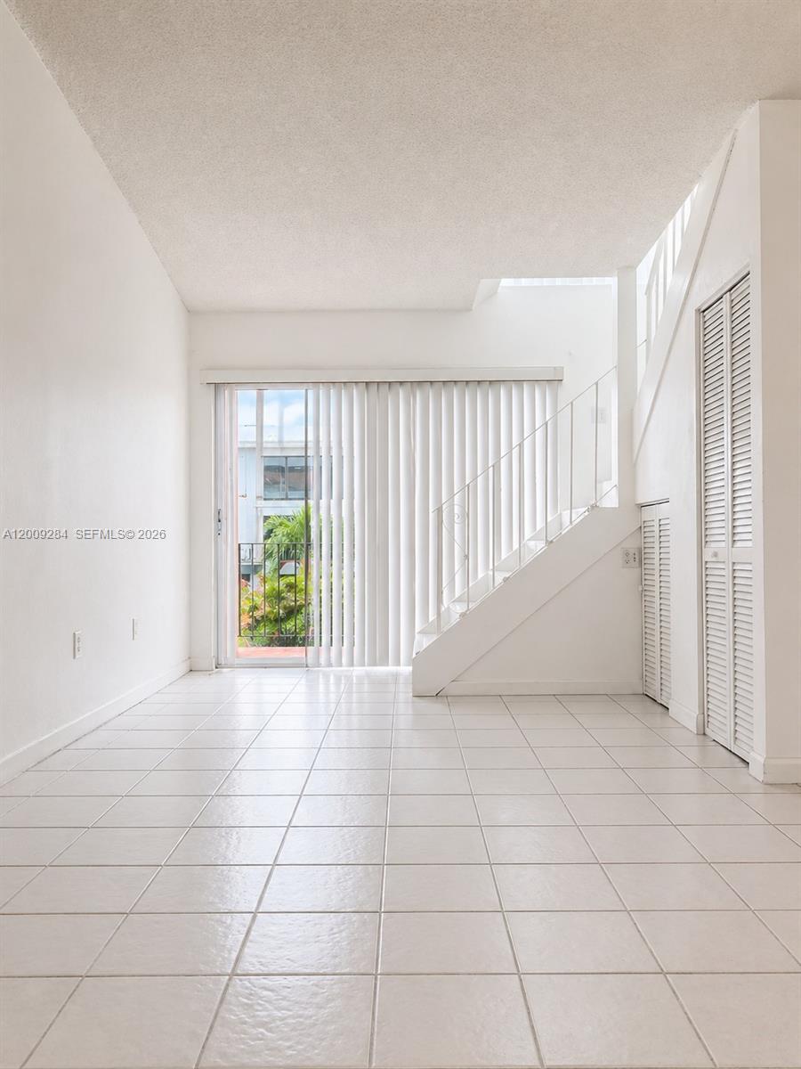 A bright living room features white tile flooring, a staircase, and a sliding glass door — 1300 W 47th Pl # 218A, Hialeah FL 33012, HIALEAH, FL