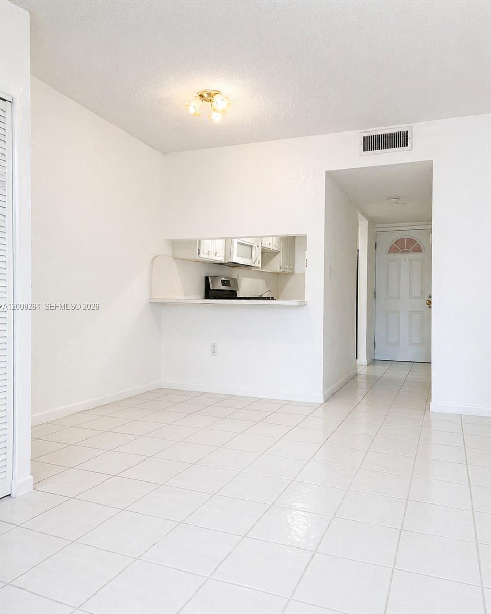 A dining area with white tile floors features a pass-through window to the kitchen — 1300 W 47th Pl # 218A, Hialeah FL 33012, HIALEAH, FL
