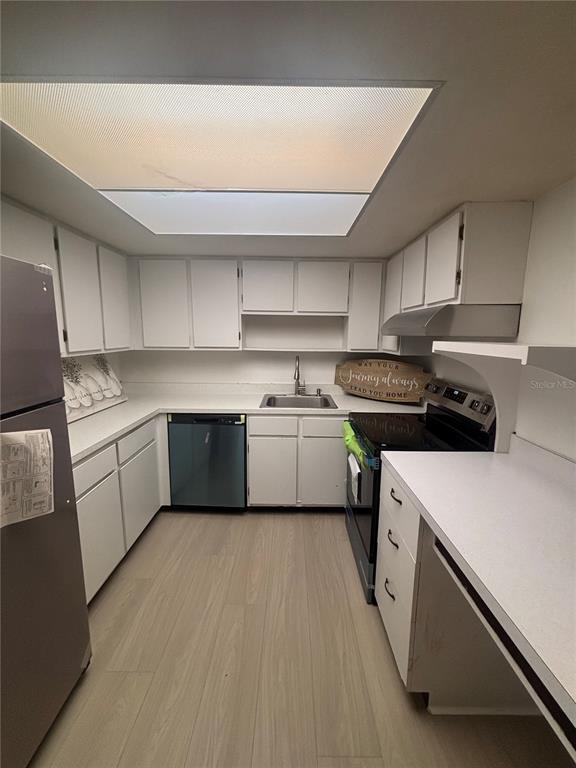 A kitchen features white cabinets, stainless steel appliances, light wood-look flooring, and a large skylight — 628 FAIRWAYS CIRCLE UNIT B, OCALA, FL