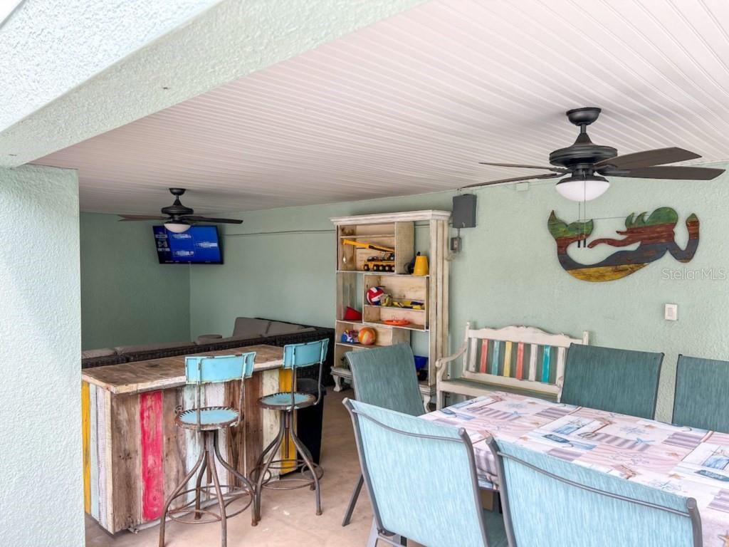 A covered outdoor patio features a bar, dining table, shelving unit, and a wall-mounted television — 308 60TH STREET UNIT A, HOLMES BEACH, FL