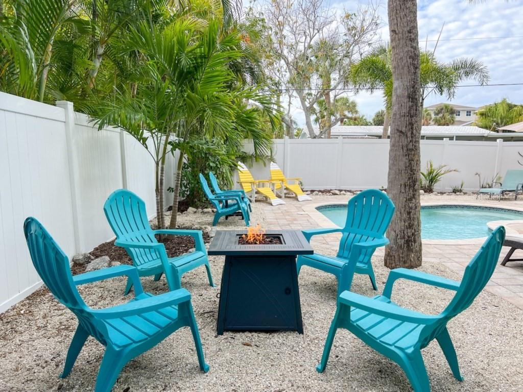 A backyard patio features a fire pit, turquoise Adirondack chairs, a pool, and palm trees — 308 60TH STREET UNIT A, HOLMES BEACH, FL