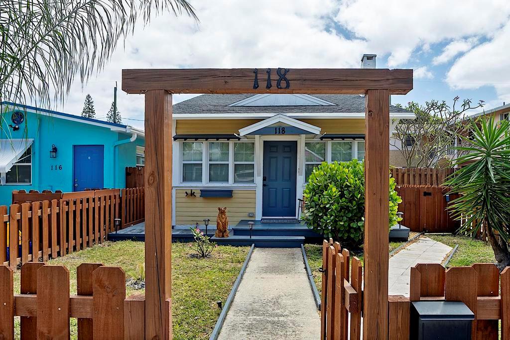 A yellow house with a blue door is viewed through a wooden arched gate — 118 S J Street, FL 33460, FL