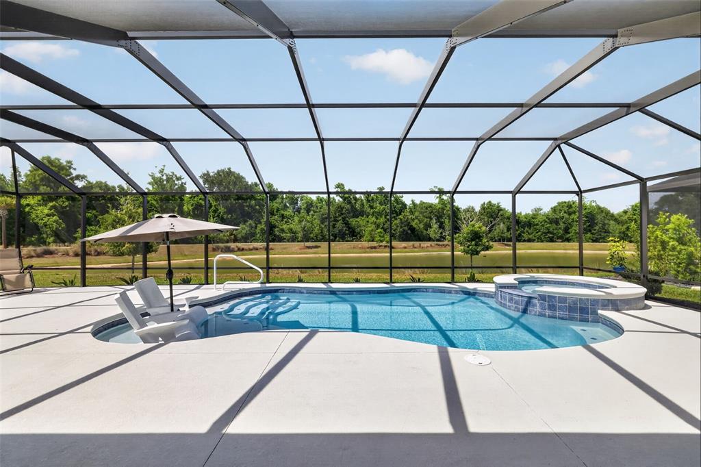 A screened-in pool area features a hot tub, lounge chairs, and a view of a pond — 6857 BAYSINGER PATH, THE VILLAGES, FL