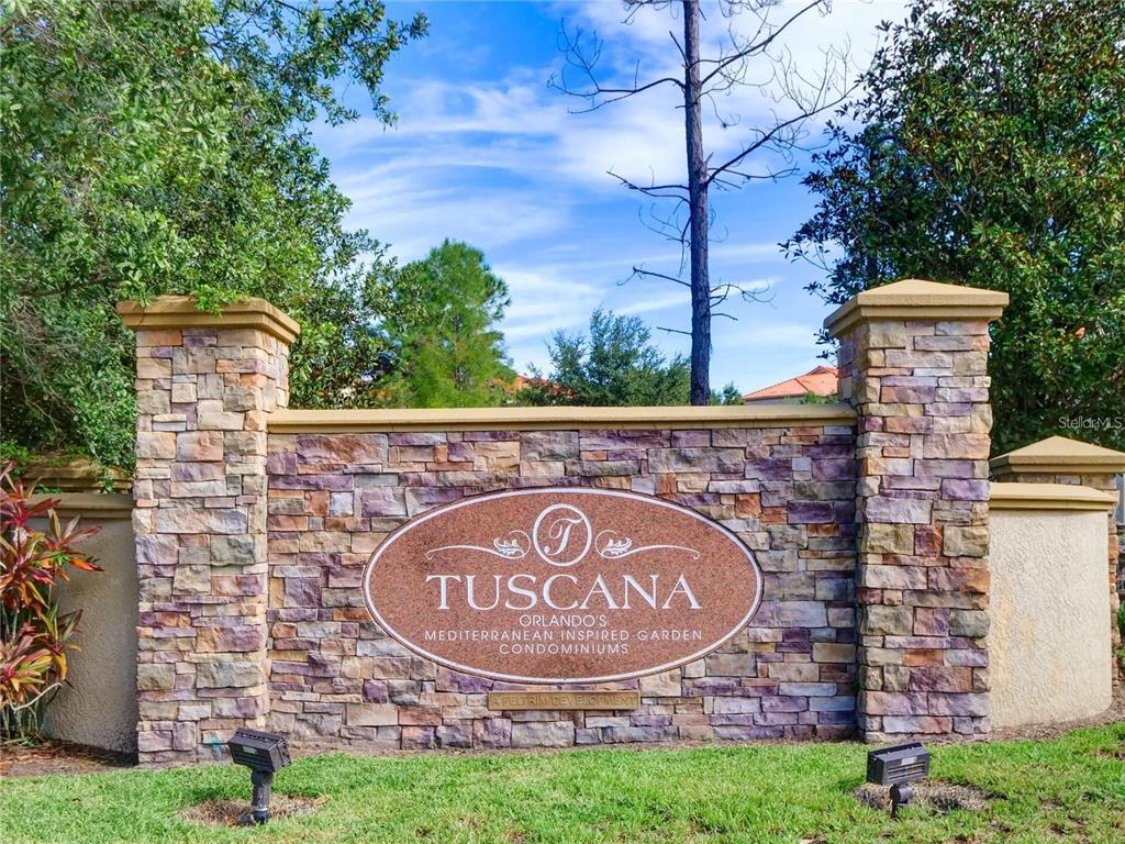 A stone monument sign for Tuscana condominiums stands in a grassy area with trees behind — 8010 TUSCANY WAY UNIT 5301, DAVENPORT, FL
