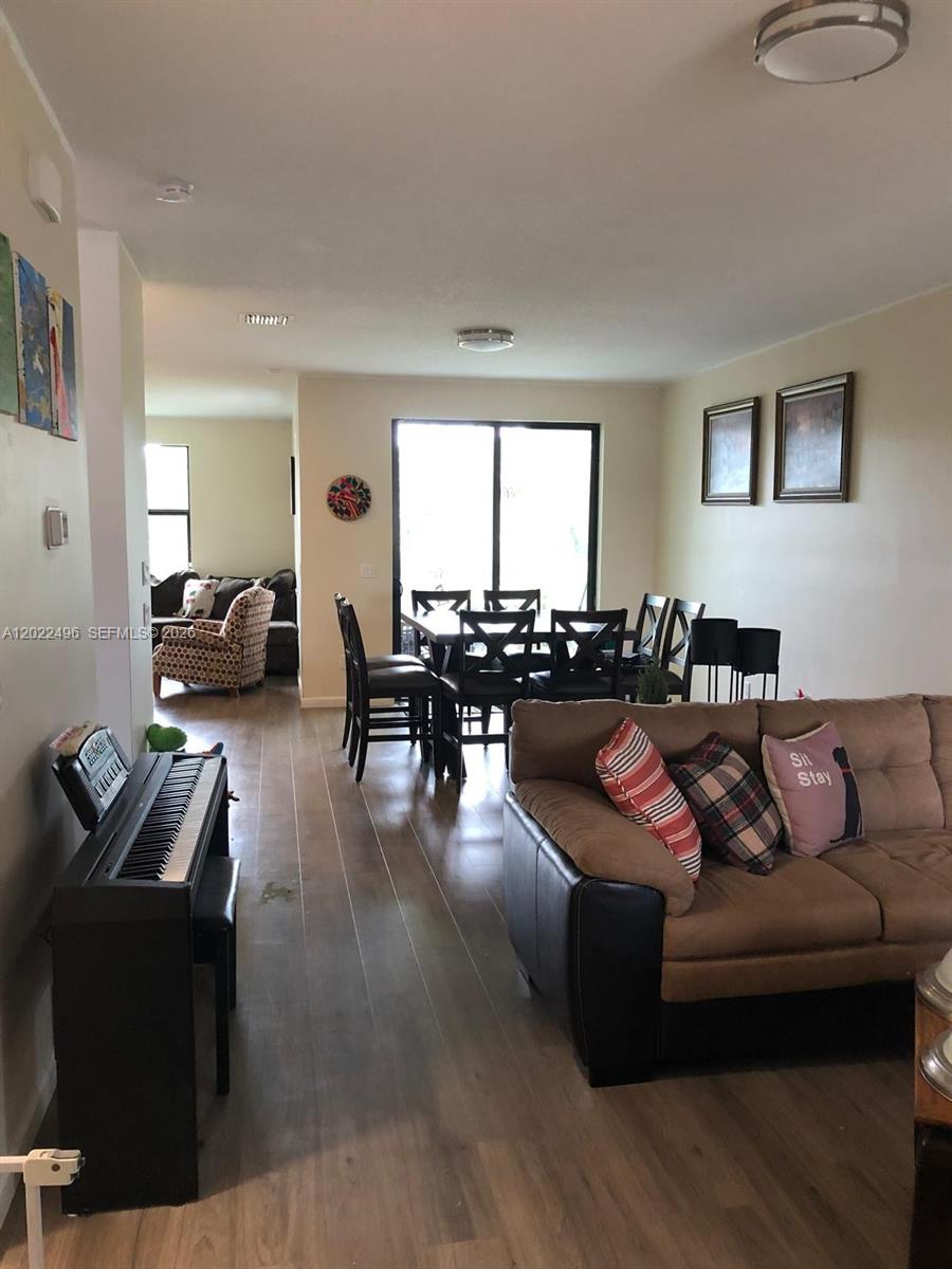 A living room with a piano, dining area, and sliding glass doors leading outside — 115 NW 36th Ave # 115, Pompano Beach FL 33069, POMPANO BEACH, FL