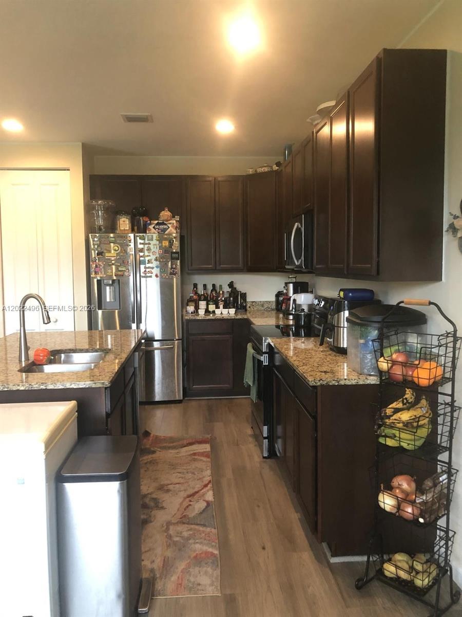 A kitchen features dark wood cabinets, granite countertops, stainless steel appliances, and light wood flooring — 115 NW 36th Ave # 115, Pompano Beach FL 33069, POMPANO BEACH, FL
