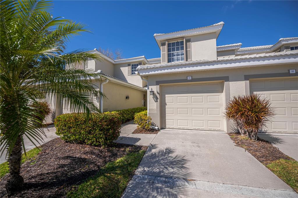 A two-story townhouse exterior with a beige stucco facade, a garage, and a palm tree — 3433 GRAND VISTA COURT UNIT 202, PORT CHARLOTTE, FL