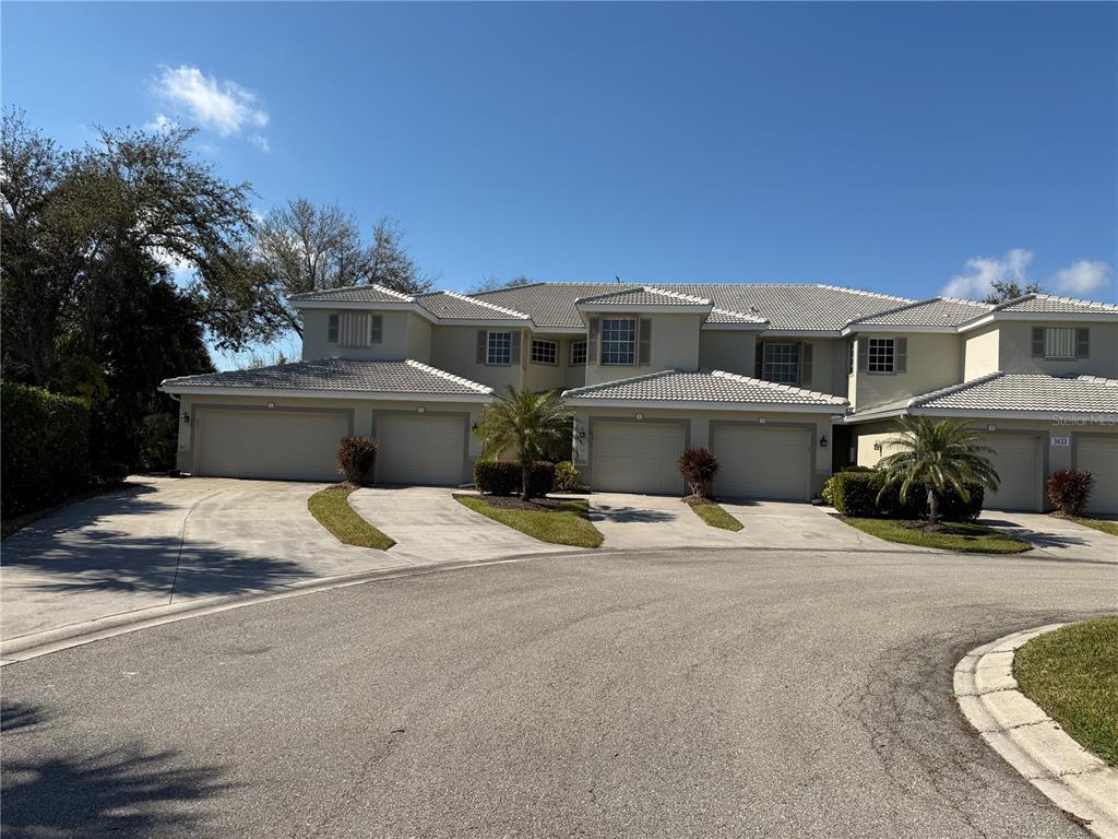 A multi-unit residential building with beige stucco walls, tiled roofs, and multiple garage doors — 3433 GRAND VISTA COURT UNIT 202, PORT CHARLOTTE, FL