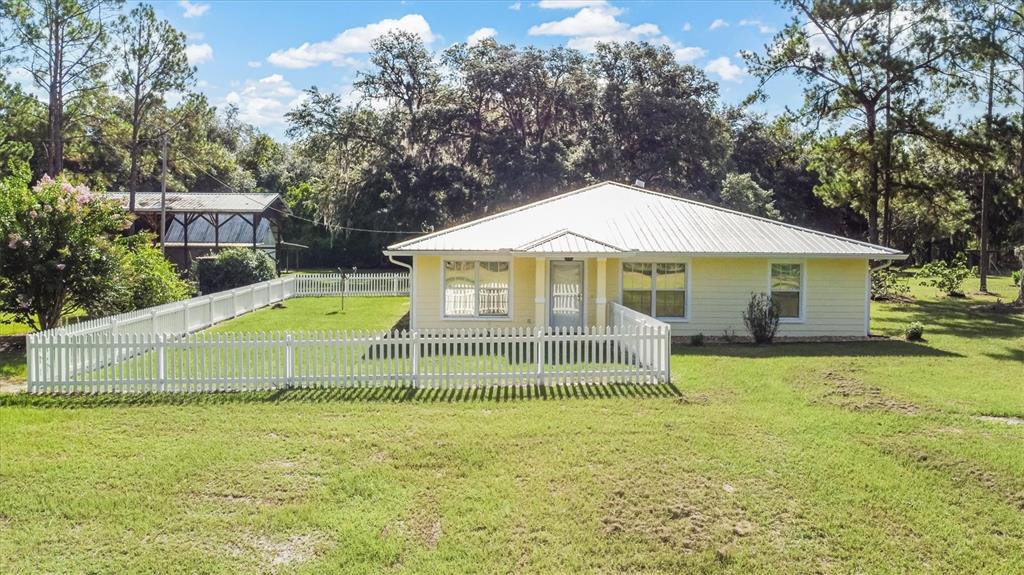 A yellow single-story house with a white metal roof sits behind a white picket fence — 17925 SE 49TH PLACE, HAWTHORNE, FL