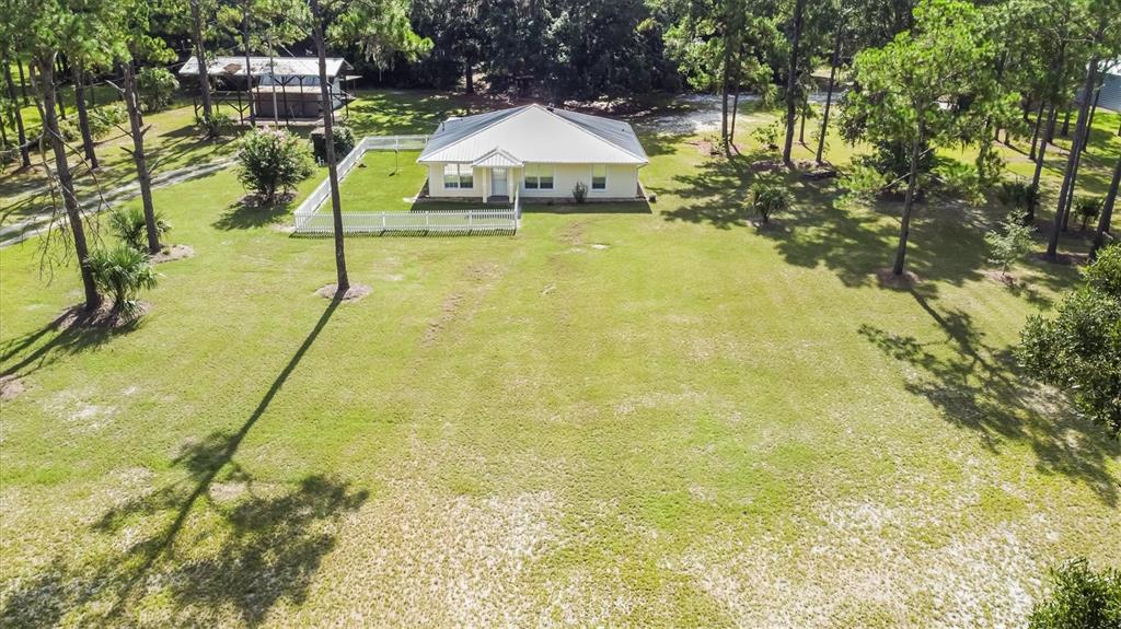 An aerial view shows a light-colored house with a metal roof inside a fenced yard — 17925 SE 49TH PLACE, HAWTHORNE, FL