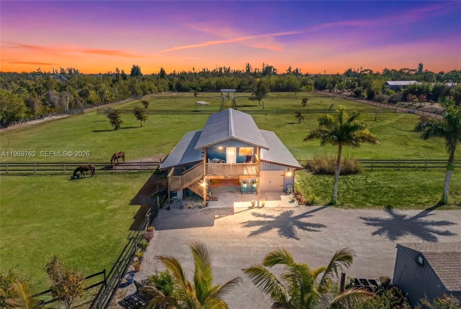 An elevated blue house with a metal roof sits on a large, fenced horse pasture — 6050 Stringfellow Rd, Saint James City FL 33956, SAINT JAMES CITY, FL