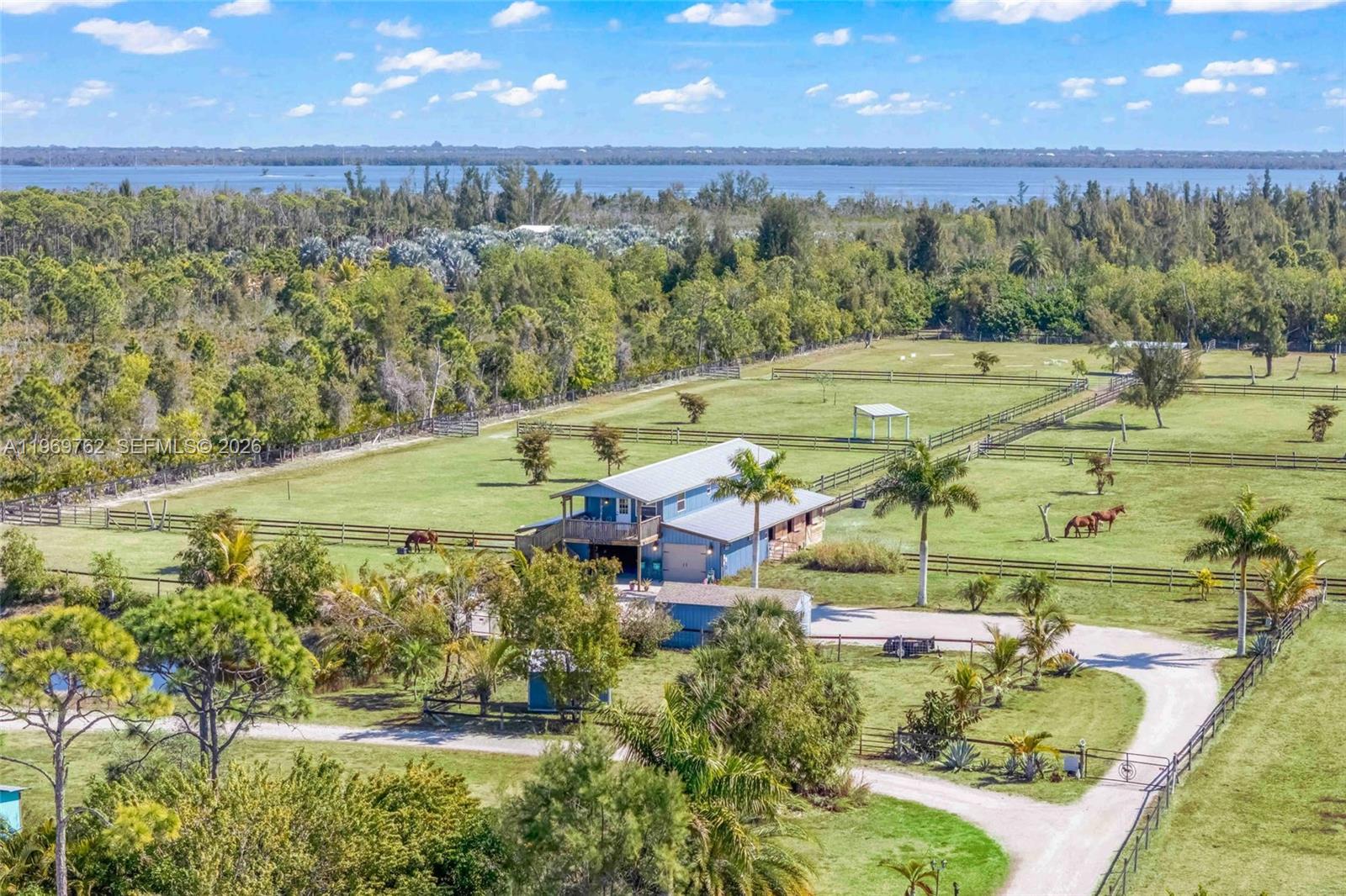 An aerial view shows a blue barn-style house on a large, fenced-in horse property — 6050 Stringfellow Rd, Saint James City FL 33956, SAINT JAMES CITY, FL