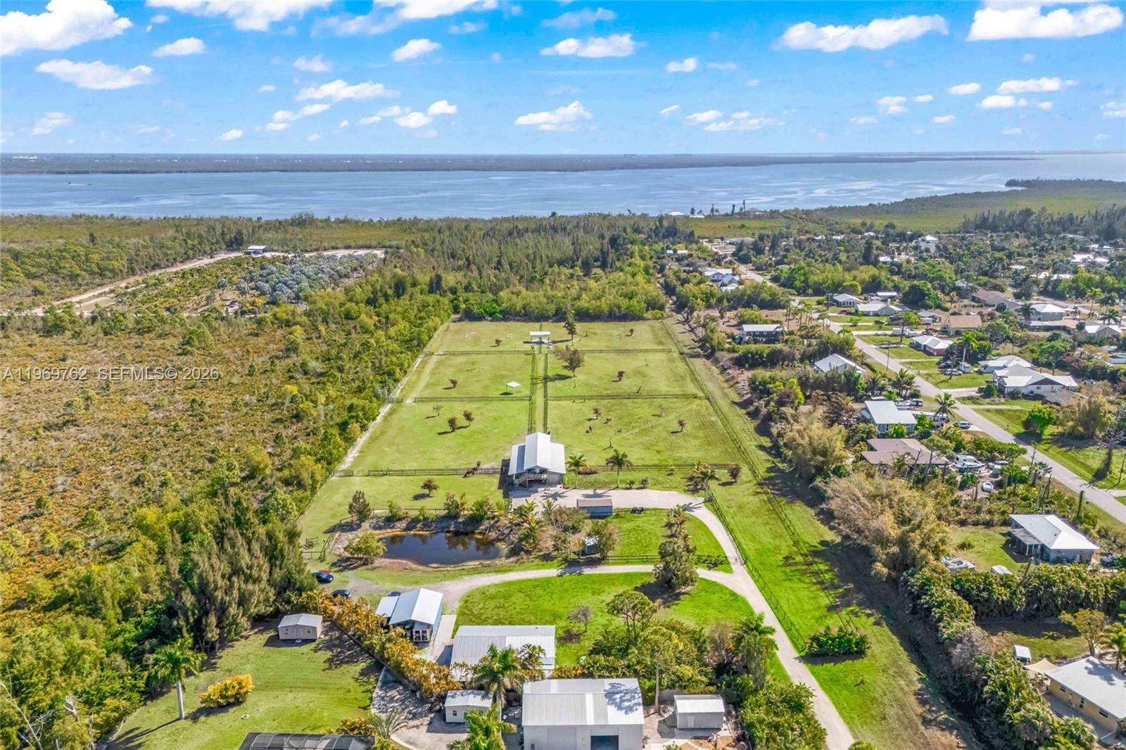 An aerial view shows a large property with multiple buildings, fenced pastures, and a pond — 6050 Stringfellow Rd, Saint James City FL 33956, SAINT JAMES CITY, FL