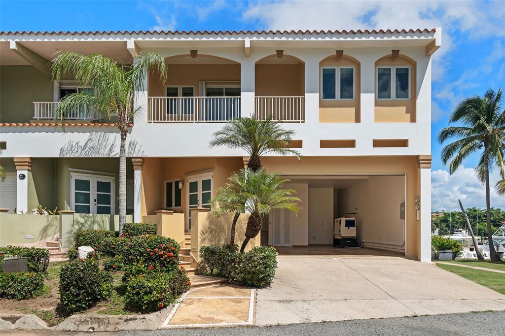 A two-story townhouse features a ground-level garage, a second-floor balcony, and landscaped front gardens — 13 SEASCAPE PENINSULA, HUMACAO, PR