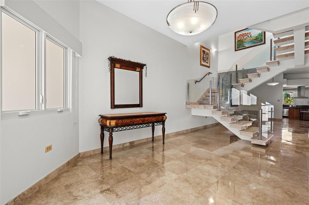 A bright entryway features marble floors, a wooden console table, and a modern floating staircase — 13 SEASCAPE PENINSULA, HUMACAO, PR