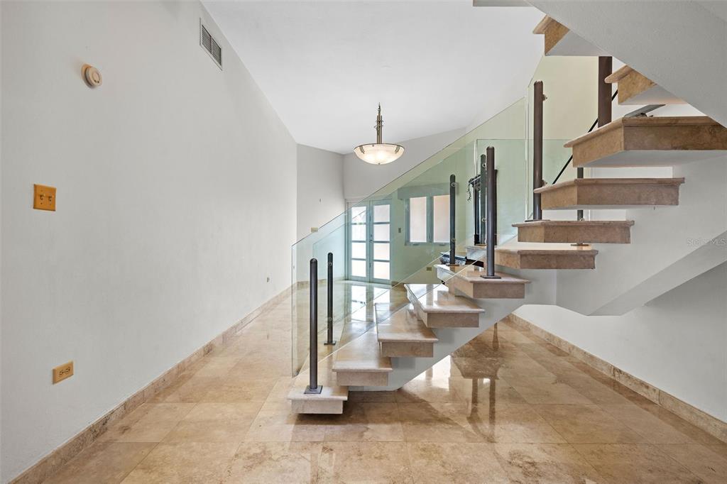 A bright entryway features a floating stone staircase with a glass railing and tile flooring — 13 SEASCAPE PENINSULA, HUMACAO, PR