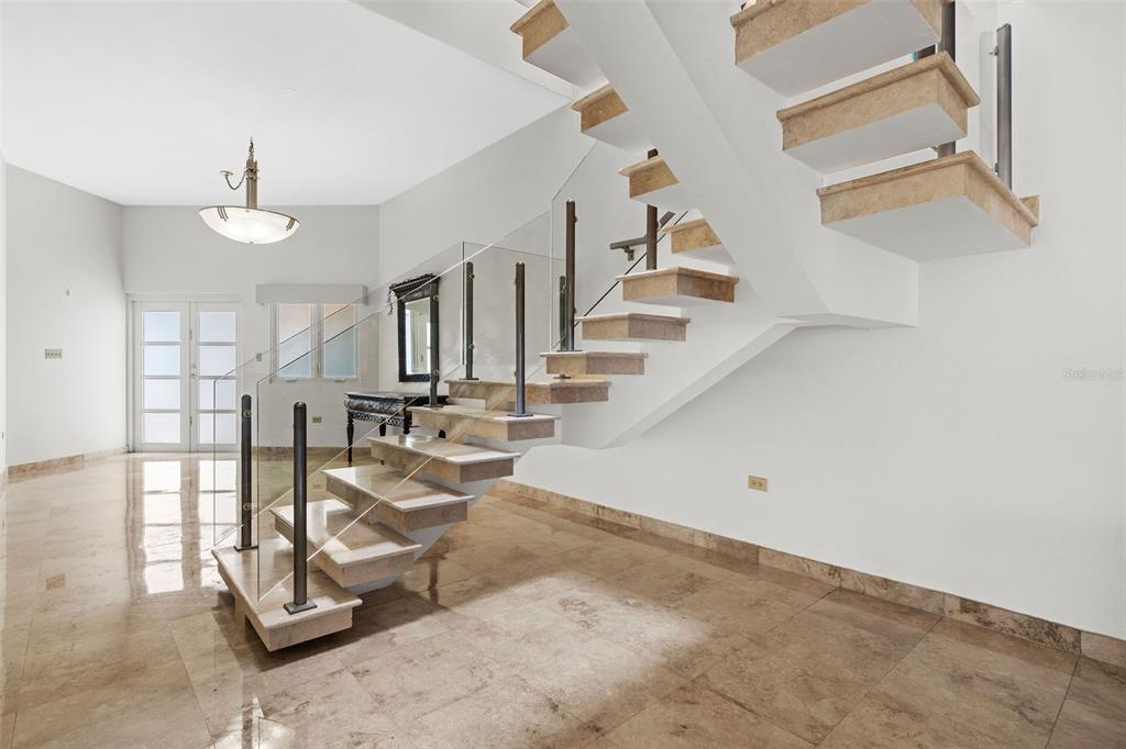 A modern staircase with stone treads and glass railings sits in a tiled entryway — 13 SEASCAPE PENINSULA, HUMACAO, PR