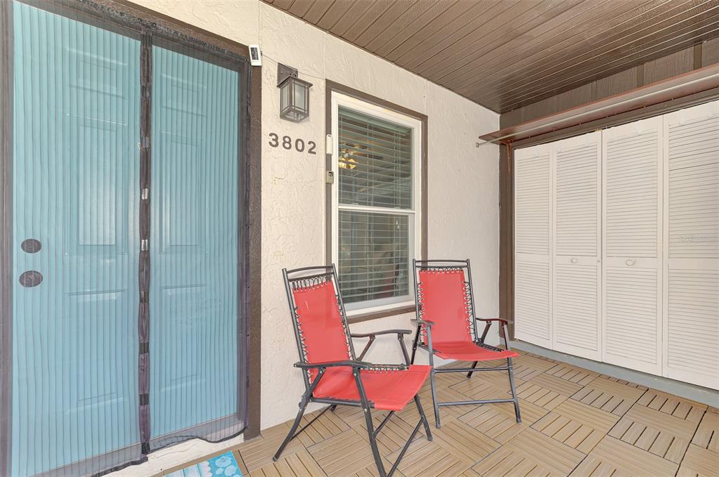 A covered patio features two red folding chairs, a blue screen door, and white shutters — 3802 59TH AVENUE W UNIT 4113, BRADENTON, FL