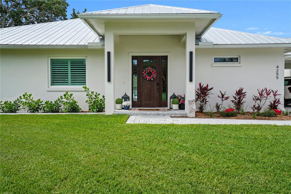 A single-story house exterior features a metal roof, white stucco walls, and a wooden door — 4255 79TH STREET, VERO BEACH, FL