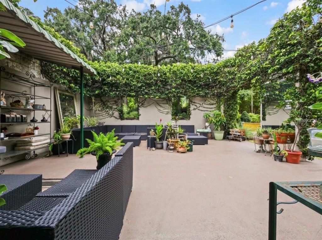 A spacious outdoor patio features black wicker furniture, potted plants, and walls covered in greenery — 4421 EDGEWATER DRIVE, ORLANDO, FL