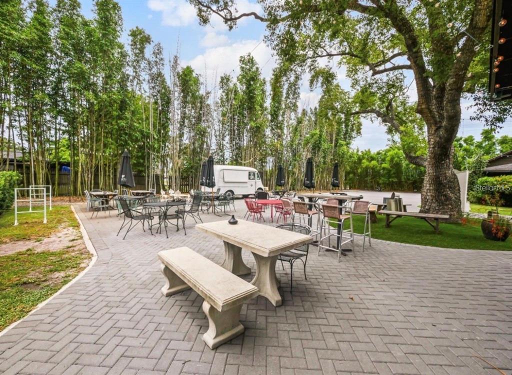 An outdoor patio features stone tables, benches, and chairs under large trees and string lights — 4421 EDGEWATER DRIVE, ORLANDO, FL