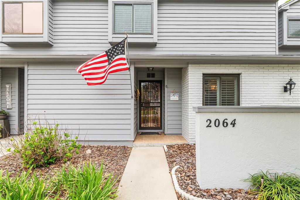 A grey two-story townhouse exterior features a front door, an American flag, and house number 2064 — 2064 SE 37TH COURT CIRCLE, OCALA, FL