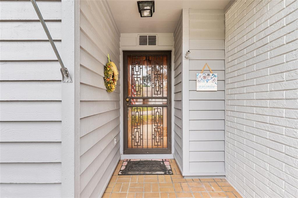 A covered entryway features a metal security door, a welcome sign, and a brick floor — 2064 SE 37TH COURT CIRCLE, OCALA, FL