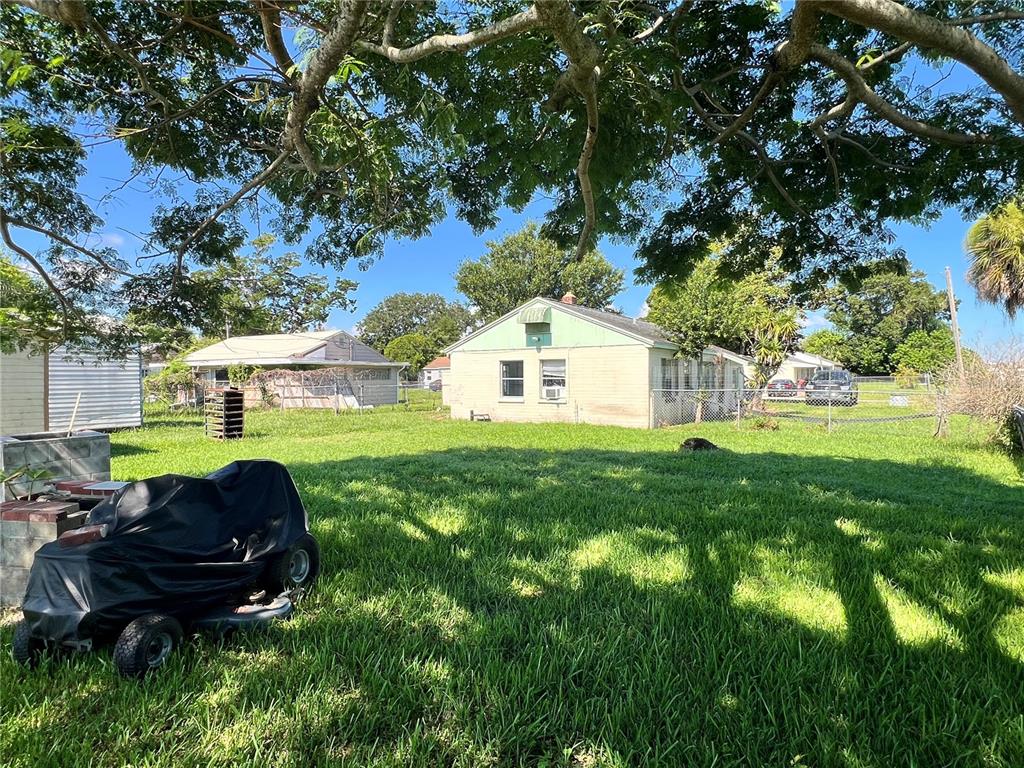 A grassy backyard features a covered lawn mower, a small house, and mature trees — 104 GRACE AVENUE, COCOA, FL