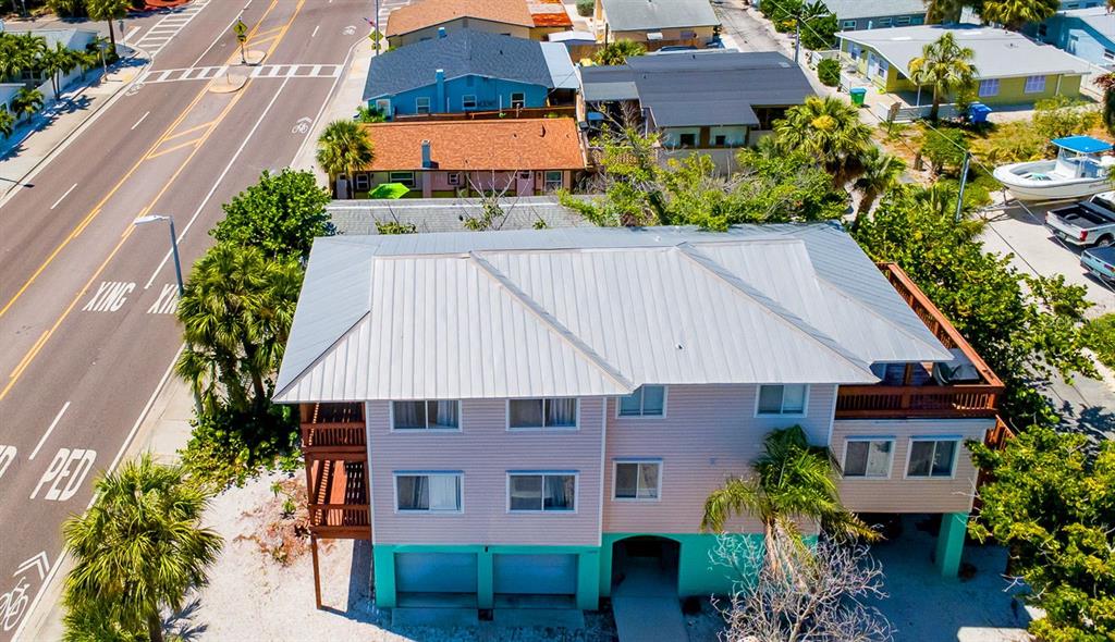 An elevated house with a metal roof, light siding, and a turquoise ground-level garage — 12201 GULF BOULEVARD, TREASURE ISLAND, FL
