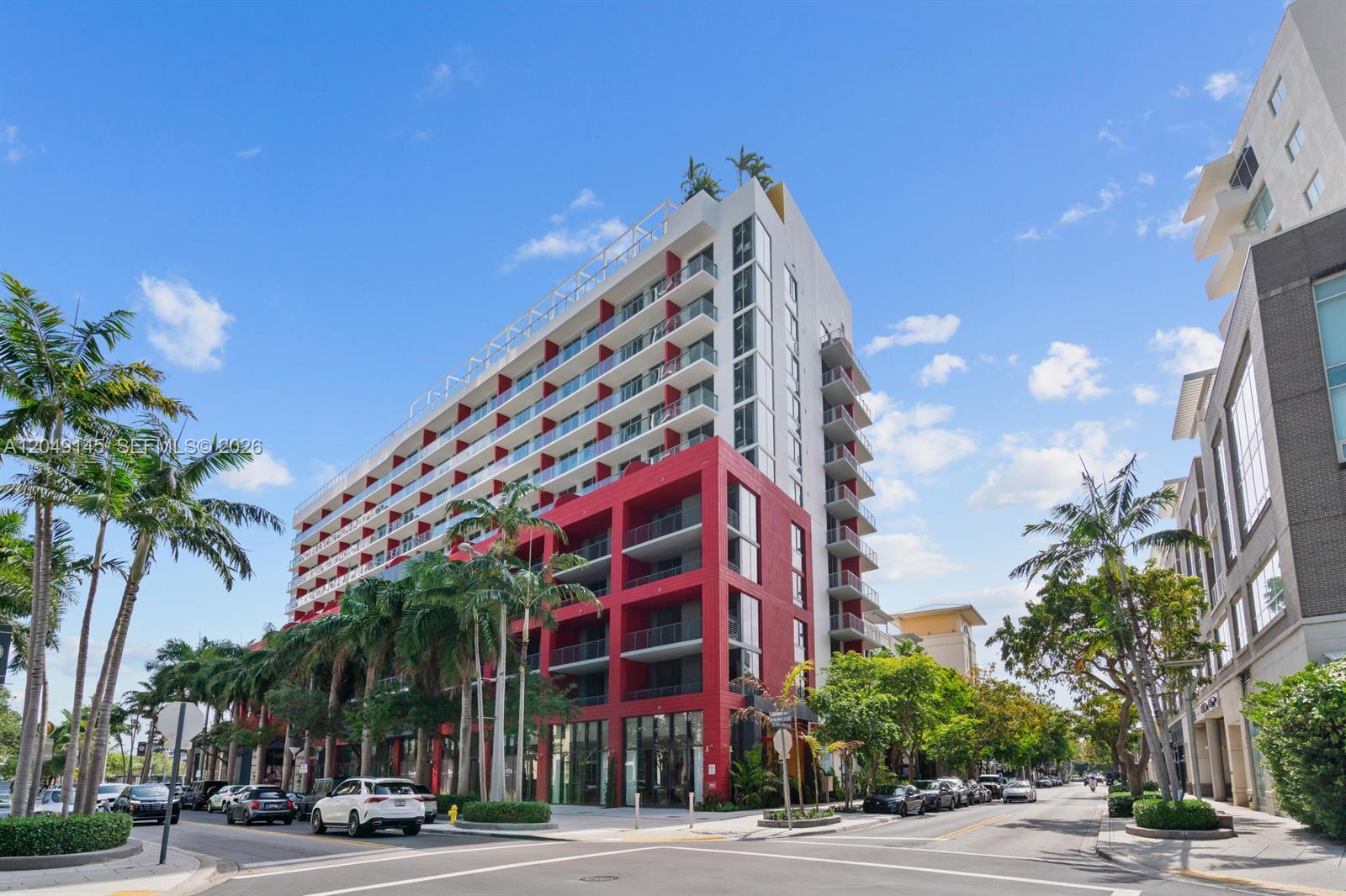 A multi-story building with a red facade and white balconies stands on a street corner — 90 NE 32nd # 727, Miami FL 33127, MIAMI, FL