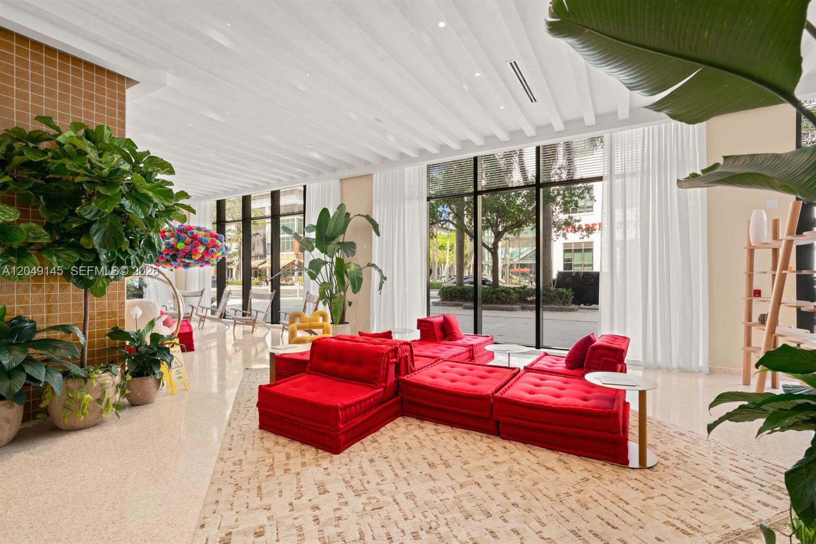 A modern lobby features red modular seating, large windows, and potted plants on a tiled floor — 90 NE 32nd # 727, Miami FL 33127, MIAMI, FL
