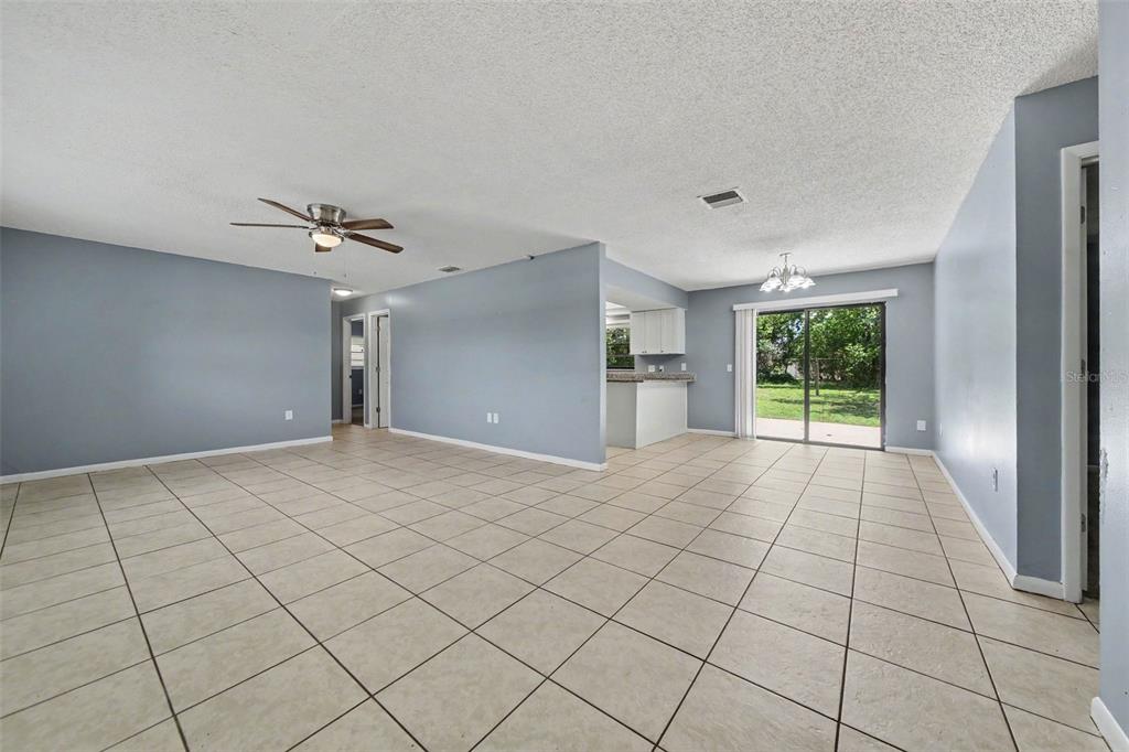 A spacious living room with light blue walls, beige tile flooring, and a sliding glass door — 840 RAYSTON STREET, DELTONA, FL