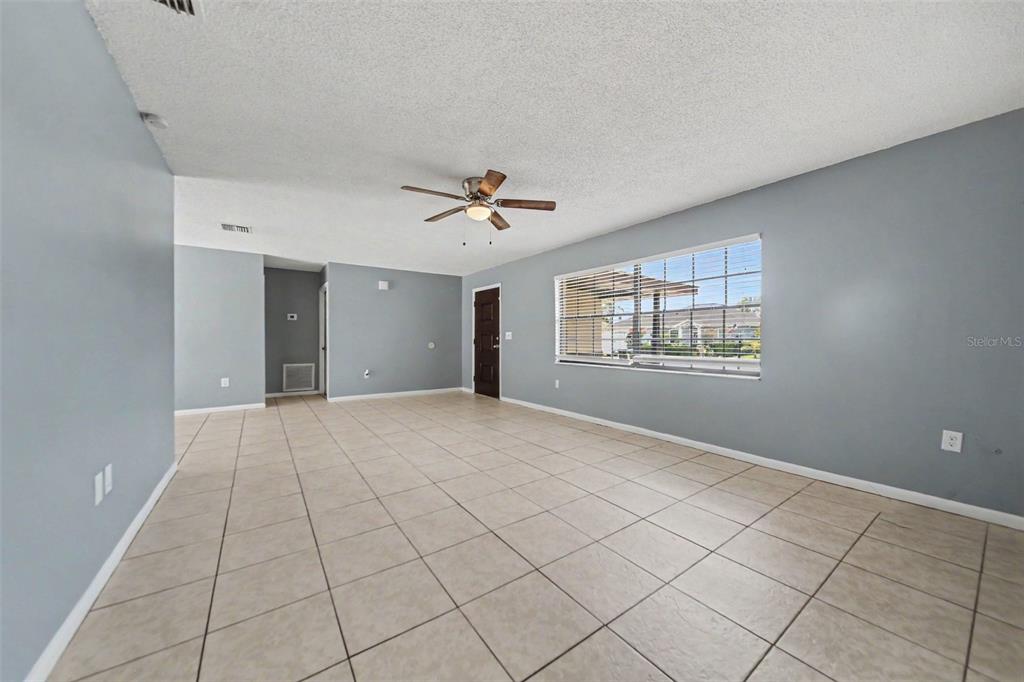 An empty living room features light blue walls, beige tile flooring, and a ceiling fan — 840 RAYSTON STREET, DELTONA, FL