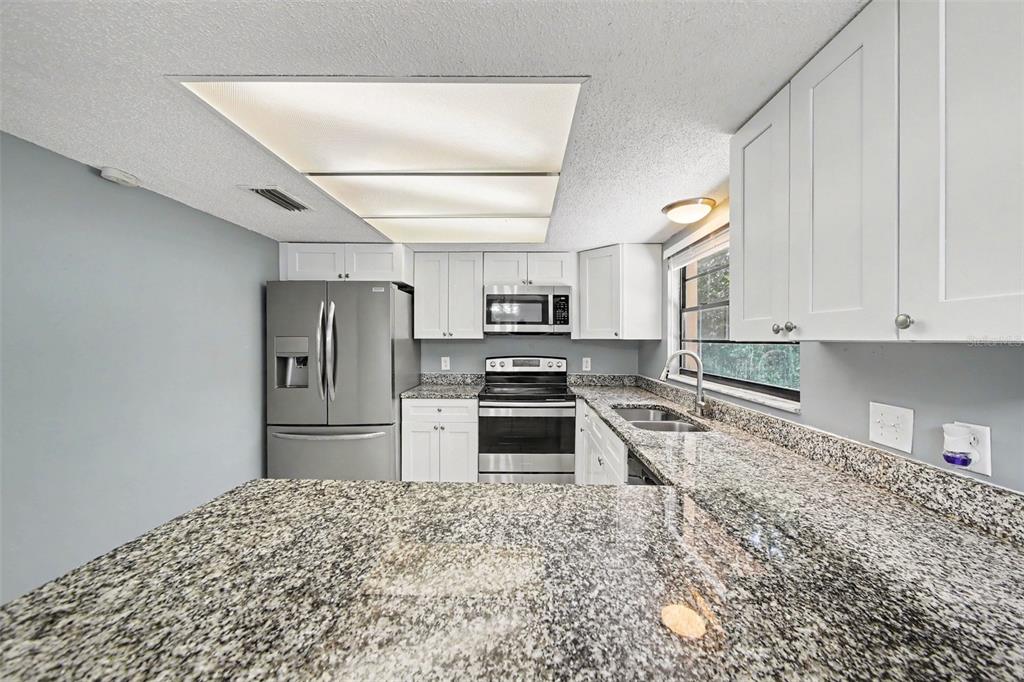 A kitchen features white cabinets, granite countertops, stainless steel appliances, and a recessed ceiling light — 840 RAYSTON STREET, DELTONA, FL