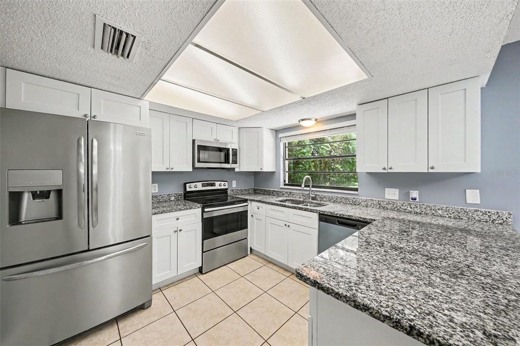 A kitchen features white cabinets, granite countertops, stainless steel appliances, and tile flooring — 840 RAYSTON STREET, DELTONA, FL
