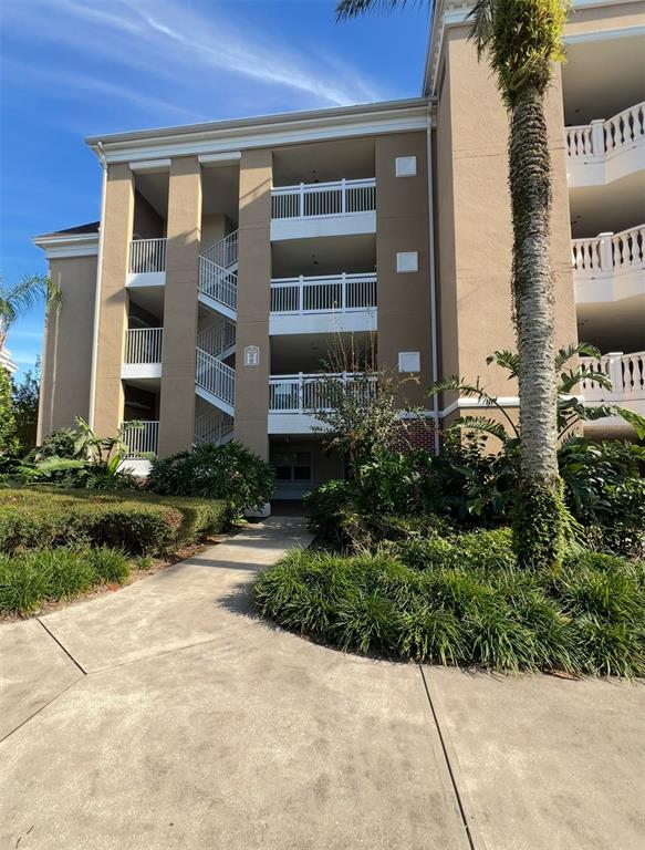 A multi-story tan apartment building features exterior staircases and white railings under a blue sky — 7612 CABANA COURT UNIT 101, REUNION, FL
