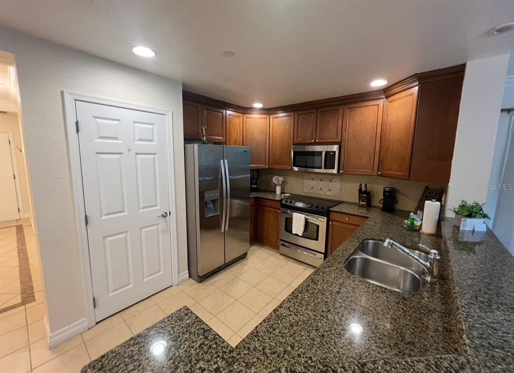 A kitchen features dark wood cabinets, granite countertops, stainless steel appliances, and tile flooring — 7612 CABANA COURT UNIT 101, REUNION, FL