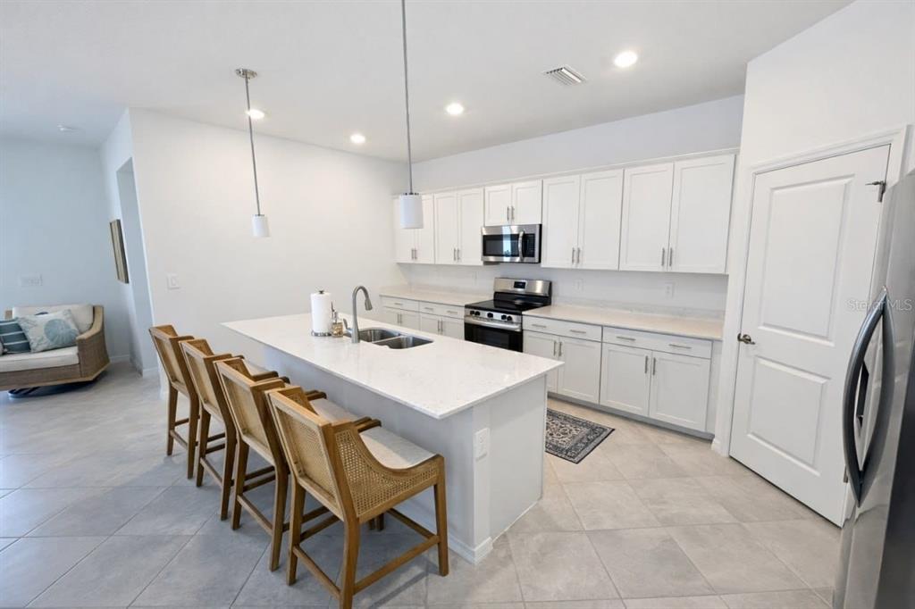 A modern kitchen features white cabinets, a large island with bar seating, and stainless appliances — 11399 PINOT DRIVE, VENICE, FL