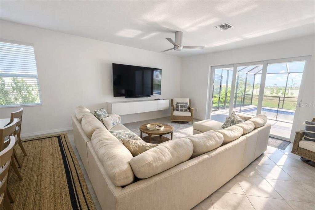 A living room features a large sectional sofa, a wall-mounted television, and sliding glass doors — 11399 PINOT DRIVE, VENICE, FL
