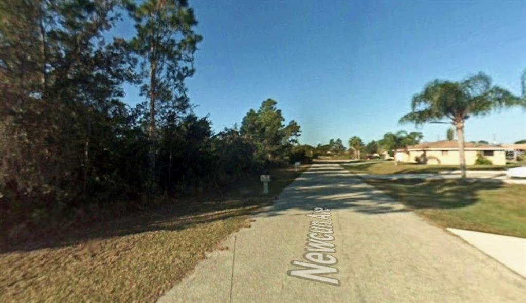 A paved street leads past a wooded lot and a residential home on a sunny day — 23105 NEWCUN AVENUE, PUNTA GORDA, FL