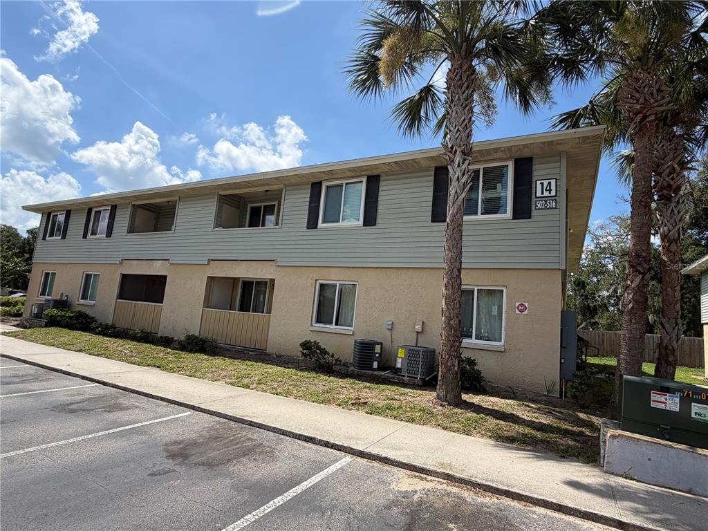 A two-story apartment building with light-colored siding and stucco exterior features a parking lot — 502 GOLDEN RAINTREE PLACE, BRANDON, FL