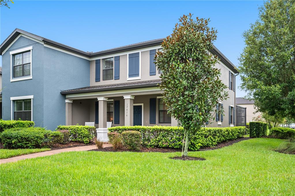 A two-story house with a covered front porch, blue shutters, and a manicured hedge — 17616 TERRAZZO WAY, LAND O LAKES, FL